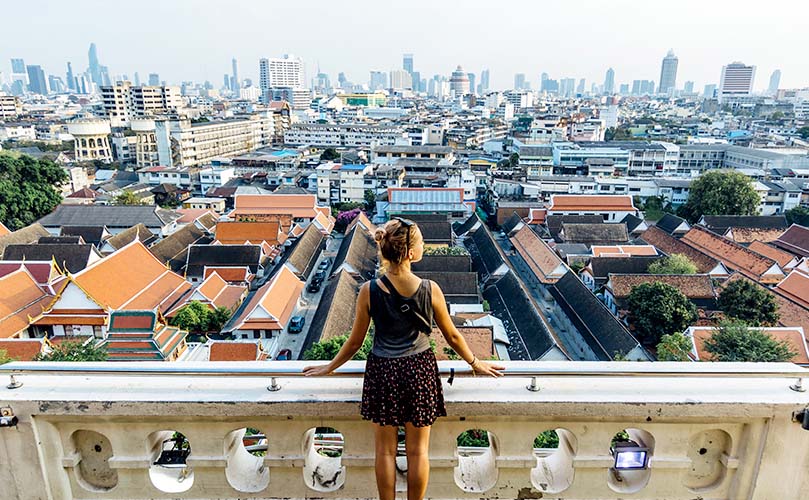  a young woman admiring the view from the Golden Mount Temple of Wat Saket towards the modern Bangkok skyline