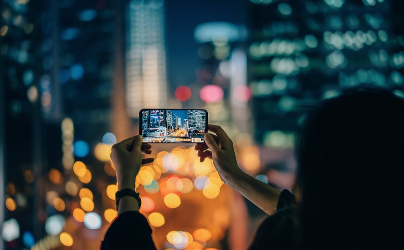A person taking a picture of a busy city at night