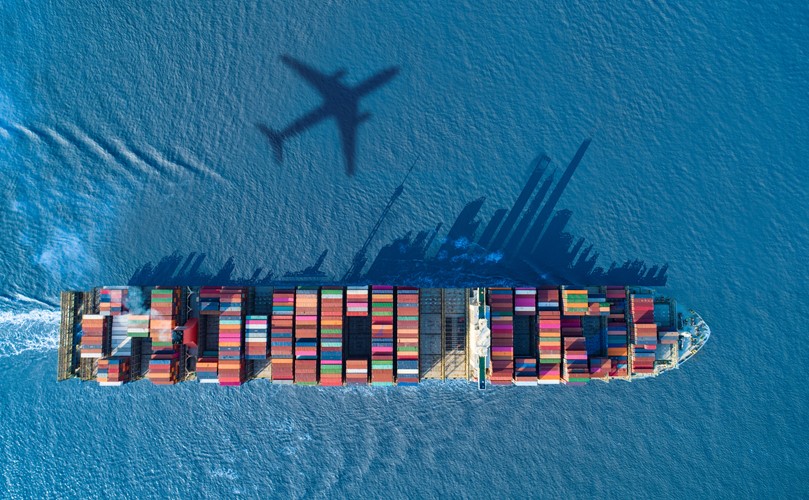 Overhead view of a cargo boat in the sea with an airplane shadow
