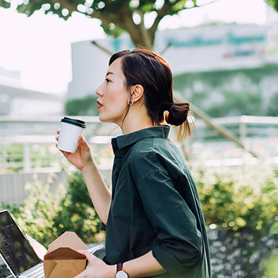 A woman sitting outside an office with a laptop and a cup of coffee