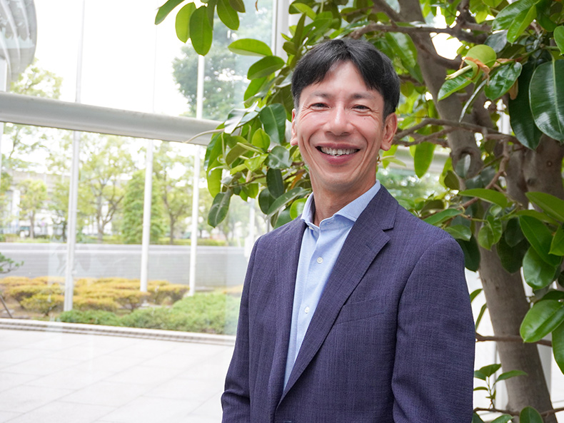富士通株式会社 技術戦略本部 コミュニケーション戦略統括部 シニアディレクター 西川 博が緑の多いオフィスの前にて、笑顔で写る写真