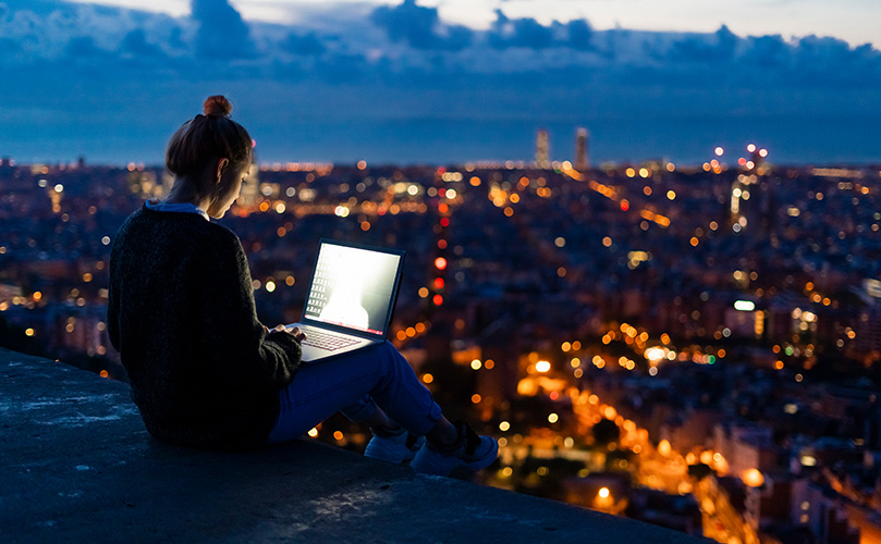 夜明けの街の上空でノートパソコンを使う若い女性
